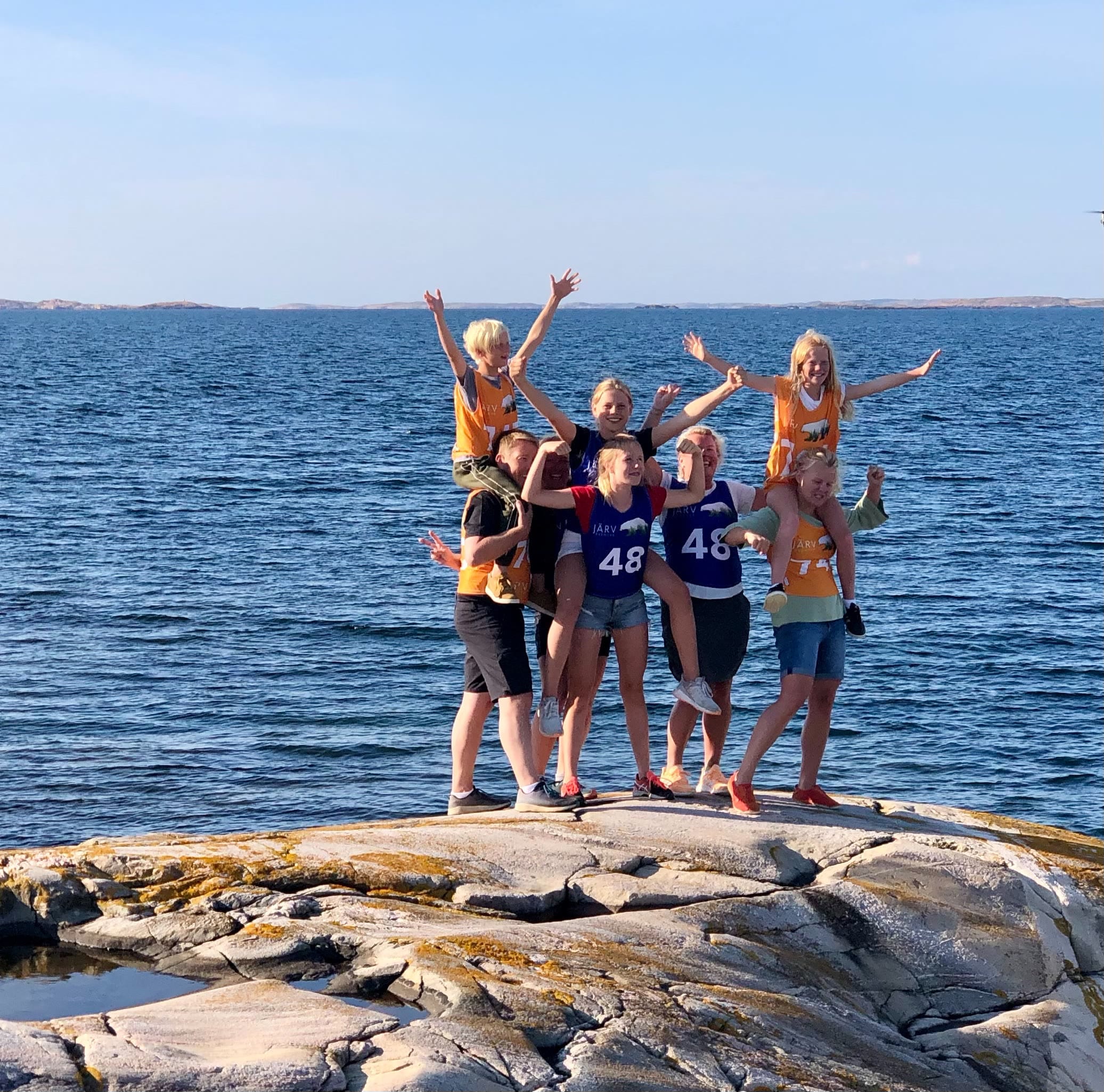 Lag i orange västar jublar på klipporna vid havet