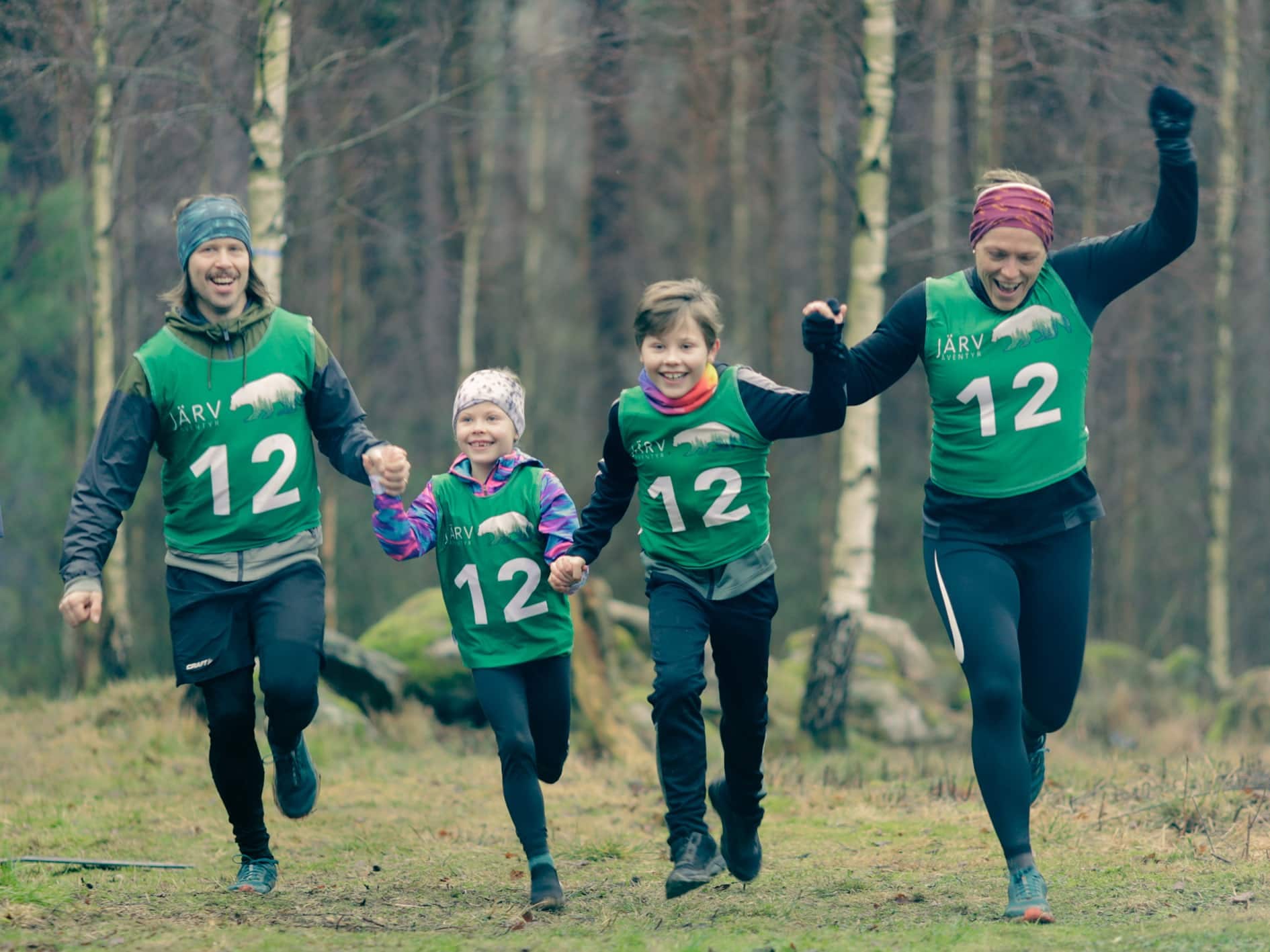 Familj i gröna västar springer hand i hand mot målet