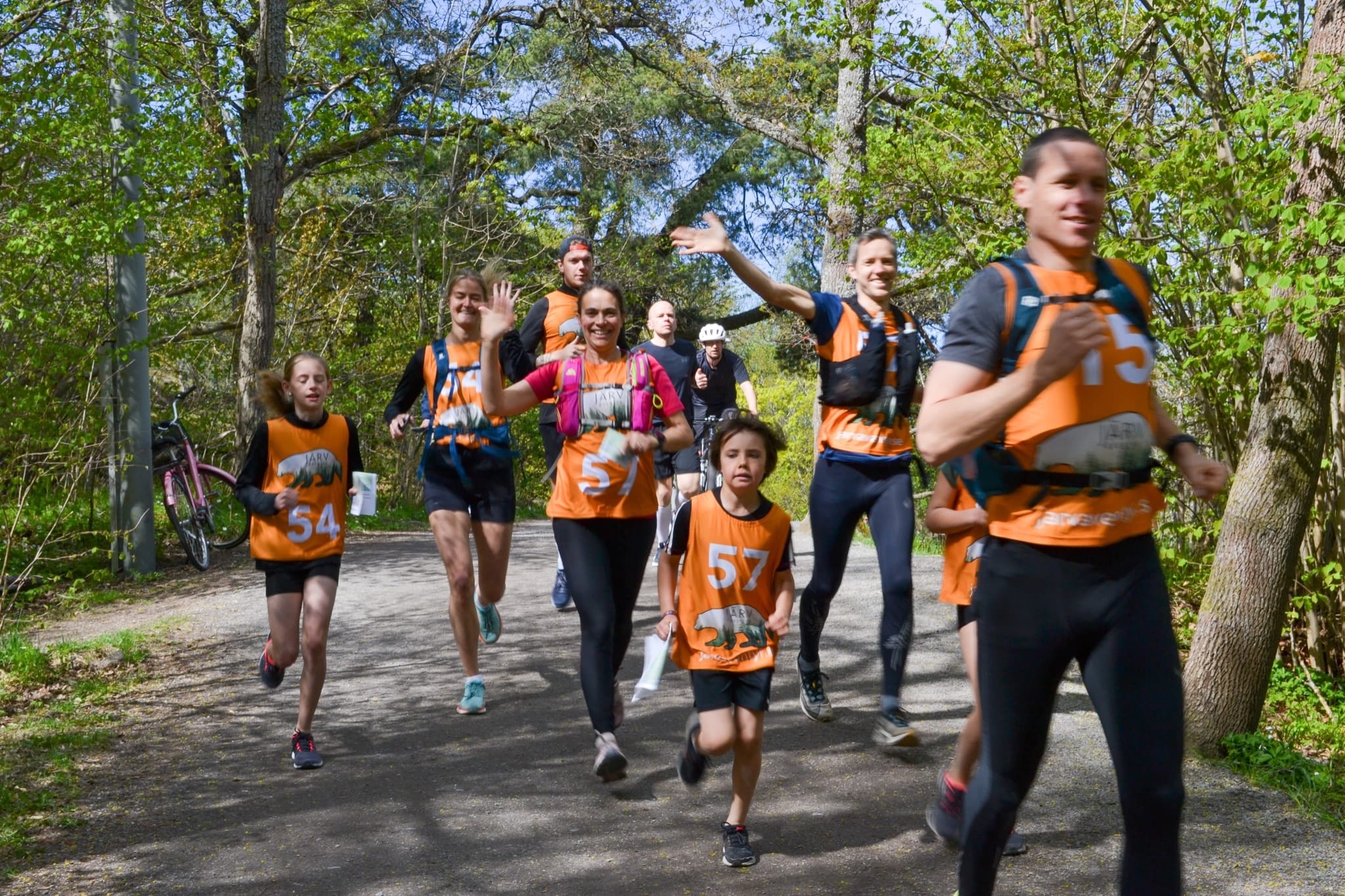Glatt gäng i orange västar springer på en grusväg genom vårgrön skog